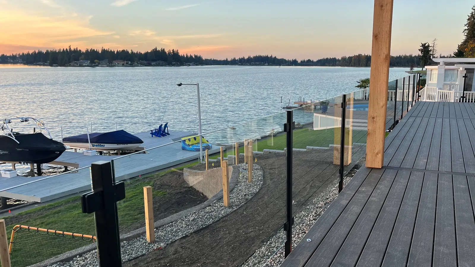 Glass railing on black posts along a lakefront deck at sunset, installed by IGo Green Enterprises in Greater Seattle