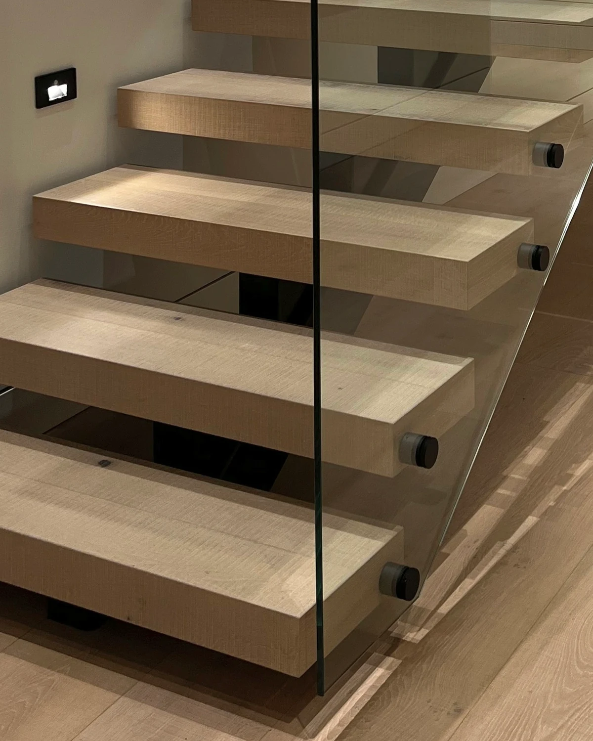 Close view of black standoffs holding frameless stair glass beside oak treads, by IGo Green Enterprises in Clyde Hill, WA